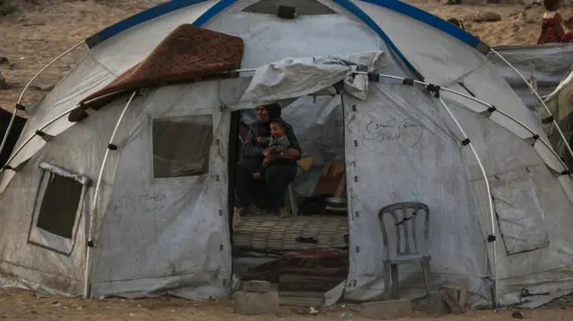 أم فلسطينية نازحة تحمل طفلها في خيمتها بميناء غزة