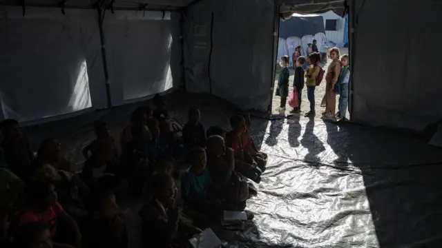 يظهر داخل الخيمة مجموعة من الطلبة دون أن تظهر ملامحهم لأن الخيمة تعتمد على ضوء الشمس من القادم من الخارج وفي الخارج طابور من مجموعة من الطلبة.