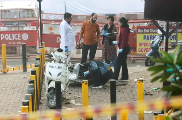 দিল্লিতে বিস্ফোরণের ঘটনাস্থলে একটি ভাঙা মোটর সাইকেলের পাশে তথ্য নিচ্ছেন নিরাপত্তা কর্মীরা, তাদের মধ্যে তিন জন নারী ও দুই জন পুরুষ