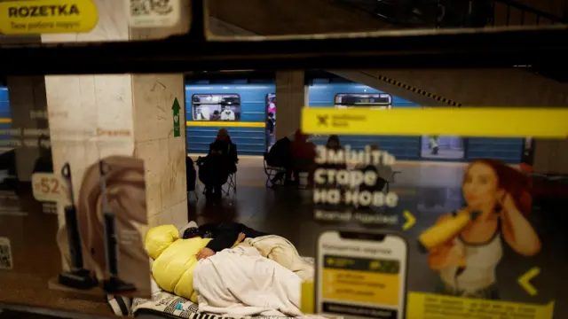 Женщина в верхней одежде лежит на полу станции метро