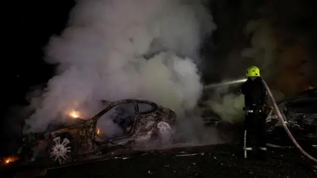 Пожарный в Харькове заливает выгоревшую и дымящуюся легковую машину