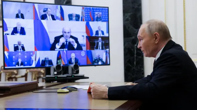 Путин сидит за столом перед экраном с множеством окон видеосвязи