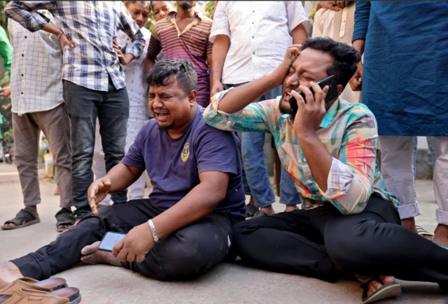 রাস্তায় বসে পা ছড়িয়ে কাঁদছেন দুই জন, তাদের একজন কানে মোবাইল ফোন ধরে আছেন। পেছনে কয়েকজন মানুষ তাদের ঘিরে দাঁড়িয়ে আছেন