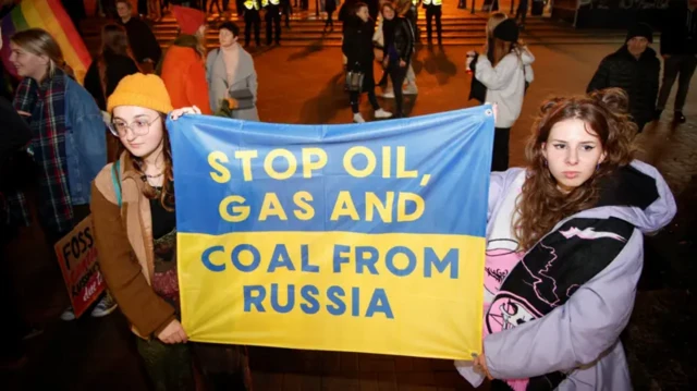 Протестующие с флагом Украины, на котором сделана надпись "прекратите поставки нефти, газа и угля из России""