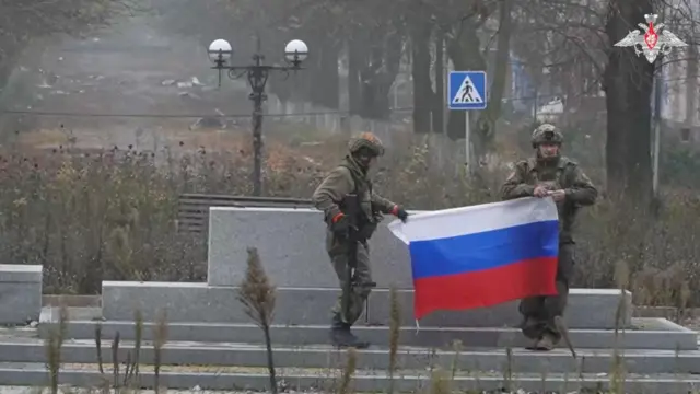 Кадр из видел с логотипом российского Минобороны, два человека в камуфляже держат российский флаг