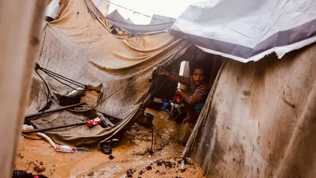 Nwata nọ n'ebe obibi ndị Palestine a chụpụrụ na Deir al-Balah, n'etiti Gaza Strip na Nọvemba 25, 2025, dịka mmiri ozuzo na-agafe n'ụlọ ntu ahụ ka agha na-aga n'ihu n'etiti Izrel na Hamas