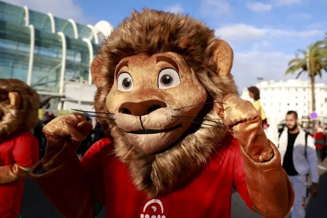 انضمّ "أسد"، شعار البطولة، إلى المشجعين والفنانين في موكبٍ مهيبٍ إلى منطقة المشجعين في الرباط، المغرب، في 20 ديسمبر/كانون الأول 2025، قبيل انطلاق بطولة كأس الأمم الأفريقية لكرة القدم.