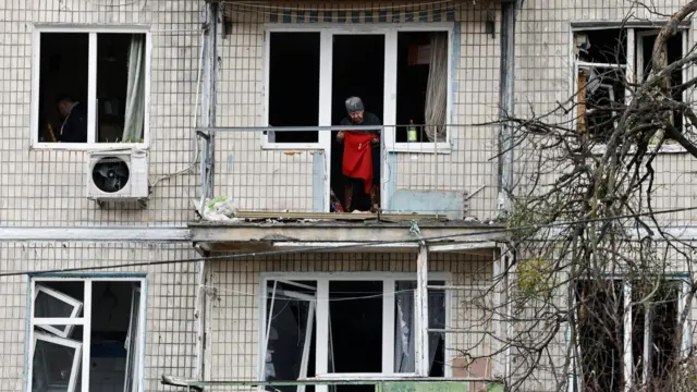 Женщина стоит у разбитого окна на одном из верхних этажей панельного дома