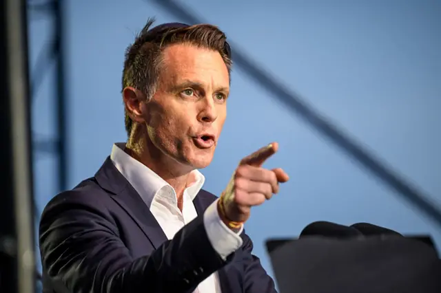 Firimiya sanye da baƙar kwat yana nuni da yatsa a lokacin zaman makoki