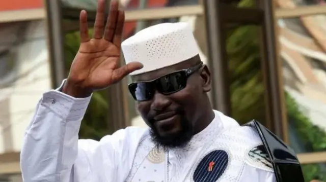 Doumbouya welili aka ya elu n'ekele ndị mmadụ dịka oyi uwe ọcha ma kpuru enyo anya nakwa okpu uwe ọcha