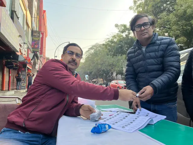 पटपड़गंज सीट पर मतदान केंद्र के बाहर पार्टी कार्यकर्ता वोटर लिस्ट के साथ