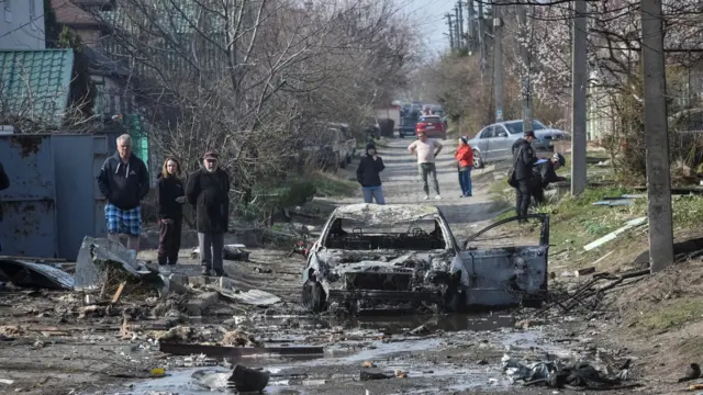 Сгоревший автомобиль на проселочной дороге, вокруг собрались люди