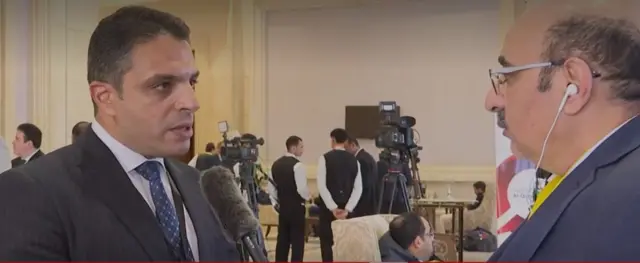 نبيل ورشدي يرتديان لباساً رسمياً، ونبيل في أذنيه سماعة