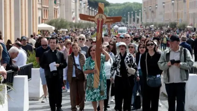 جمع من المعزين تقودهم امرأة تحمل صليباً