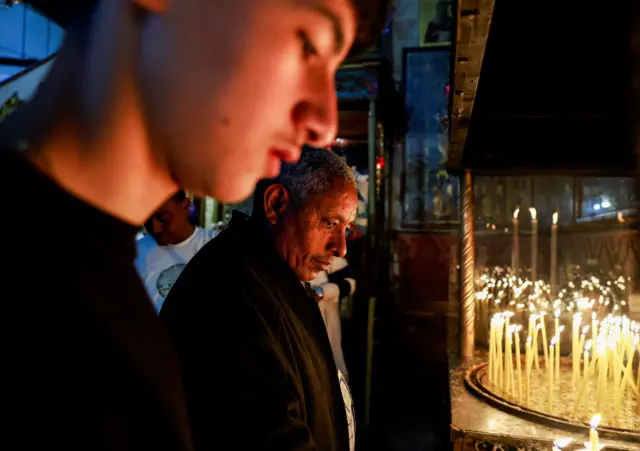 يقف الناس بجوار الشموع المضاءة داخل كنيسة المهد، بعد إعلان الفاتيكان عن وفاة البابا فرانسيس، في بيت لحم بالضفة الغربية المحتلة في 21 أبريل/نيسان 2025