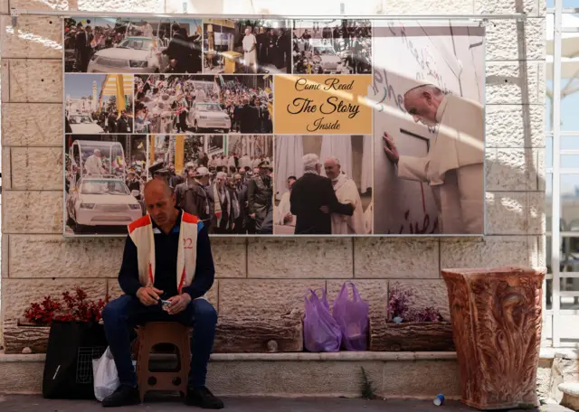 رجل يجلس أمام صور البابا فرانسيس المعروضة على الحائط، بعد إعلان الفاتيكان عن وفاة البابا فرانسيس، في مدينة بيت لحم، في الضفة الغربية المحتلة، 21 أبريل/نيسان 2025