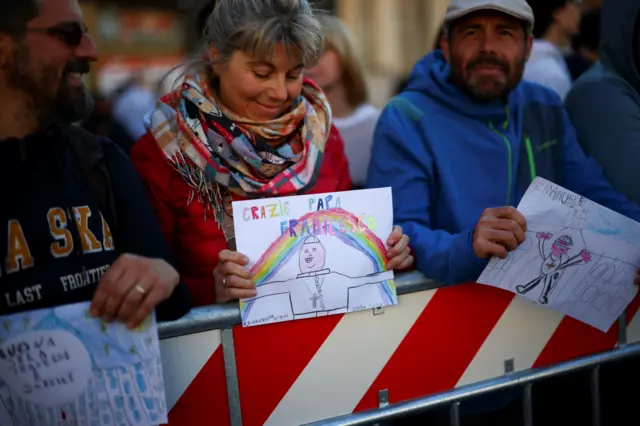 Три человека у заграждения с рисунками папы Франциска