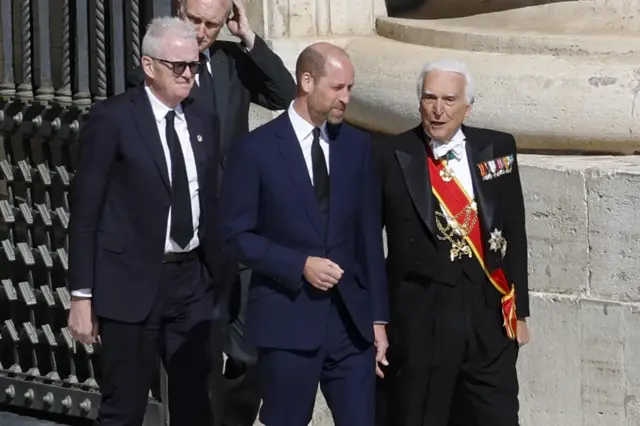 Принц Уильям в окружении двух мужчин.