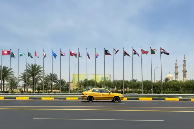 سيارة أجرة تمر أمام أعلام الدول الأعضاء في جامعة الدول العربية المرفوعة في أحد الشوارع قبل انعقاد القمة العربية الرابعة والثلاثين في بغداد