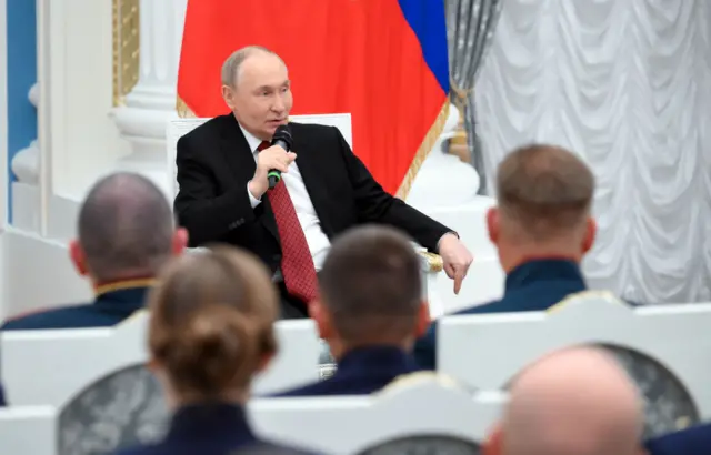 Путин говорит в микрофон перед рядами людей в парадной военной форме