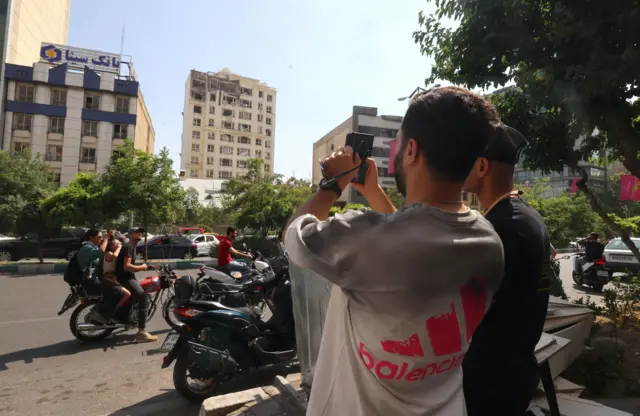 إيراني يتلقط صورة لمبنى تضرر في غارة إسرائيلية على طهران في 13 يونيو 2025.