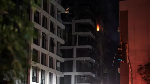 В окне на одном из верхних этажей многоэтажного дома видно пламя