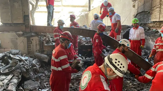 رجال إنقاذ يعملون في موقع غارة جوية ببزات حمراء وخوزات وسط كتل دمار