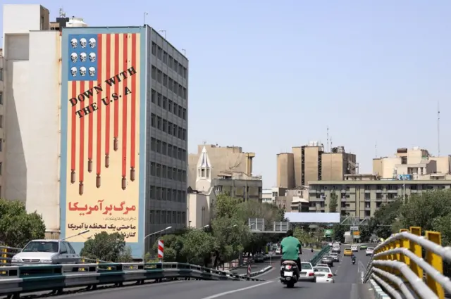 حركة مرورية بجانب مبنى عليه جدارية مناهضة للولايات المتحدة في طهران، إيران، 22 يونيو/حزيران 2025