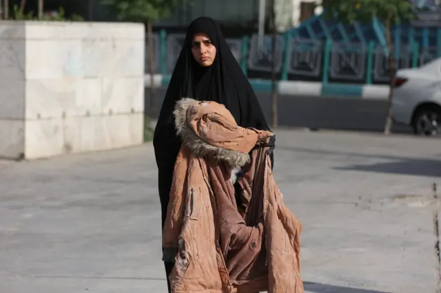 A woman holds the clothes of one of the victims of the Israeli attacks, in a street in Tehran