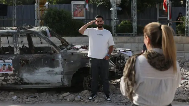 A man poses for a photo next to an ambulance burned by Israeli attacks, on a street, amid the Iran-Israel conflict, in Tehran