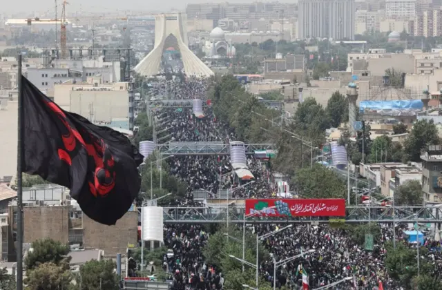 التقطت الصورة من مكان مرتفع ويظهر في الأسفل موكب كبير وحشد من الناس