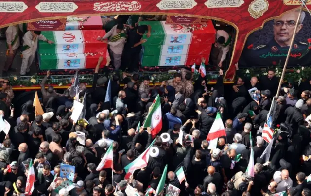 جموع من المشيعين يحملون الأعلام الإيرانية وهناك صورة للراحل رئيس هيئة الأركان اللواء محمد باقري الذي قتل في الصراع الأخير بين إسرائيل وإيران