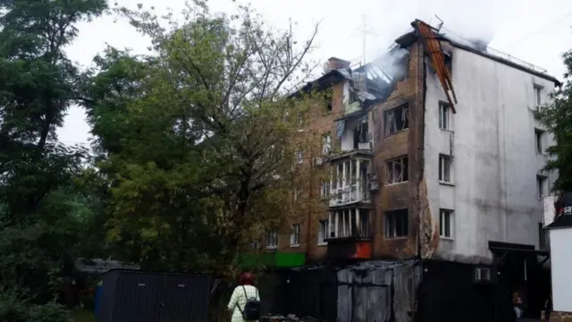 रूसी ड्रोन हमले में क्षतिग्रस्त कीव स्थित एक आवासीय इमारत को देखती एक महिला.