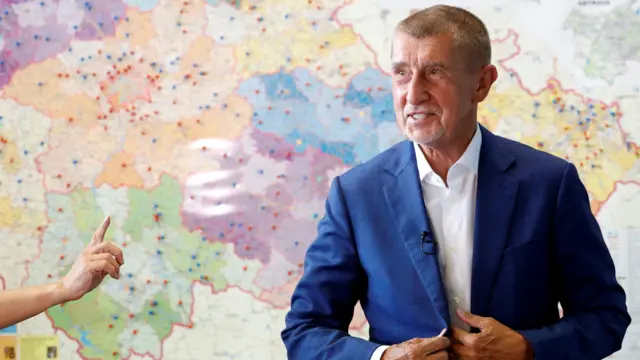 Андрей Бабиш застегивает пиджак на фоне висящей на стене карты