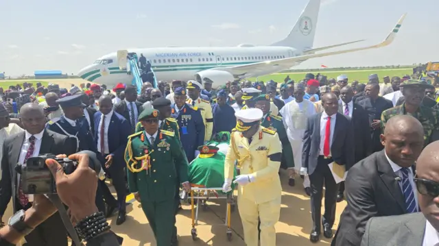 Military officials gada holding a casket wit Nigeria flag wit airplane for background