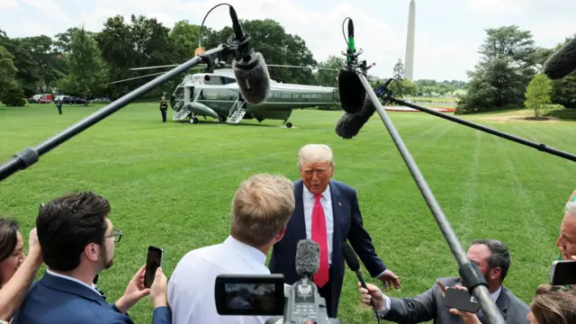 Дональд Трамп говорит в микрофоны журналистов, стоя перед вертолетом