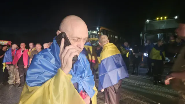 Мужчина, накрывшийся украинским флагом, говорит по мобильному телефону