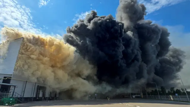 Клубы черного дыма поднимаются от здания складского или производственного назначения