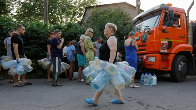 Люди несут большое количество пластиковых бутылей к автоцистерне