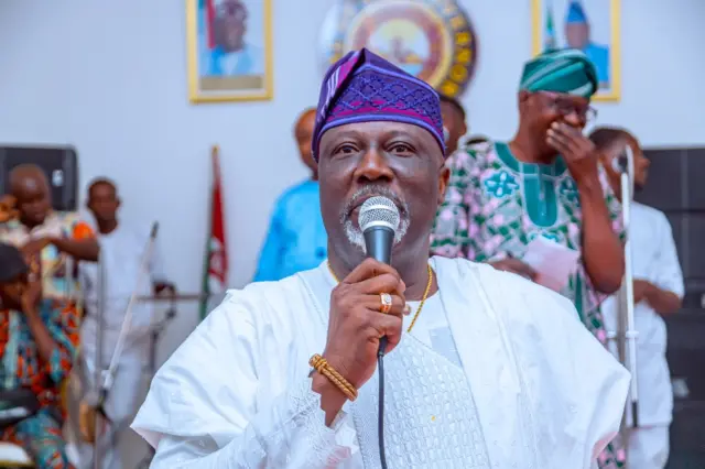 Dino Melaye riƙe da makirfo yana jawabi sanye da fararen kaya da hula mai launin cancan-bali