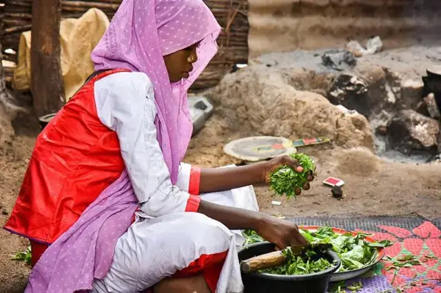 Wata mata sanye da tufafi masu launin fari da ratsin ja da mayafi mai launin ruwan hoda tana yanka ganye