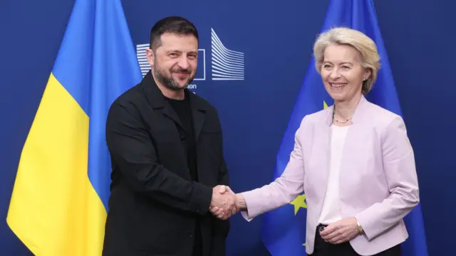 Владимир Зеленский и Урсула фон дер Ляйен жмут руки на фоне флагов ЕС и Украины