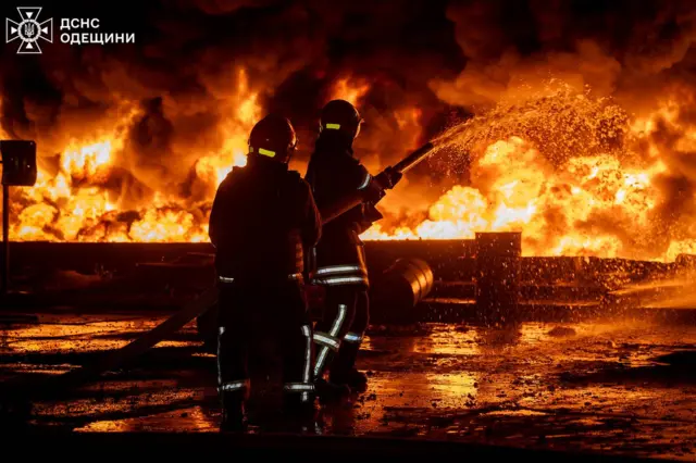 Двое пожарных тушат огонь.