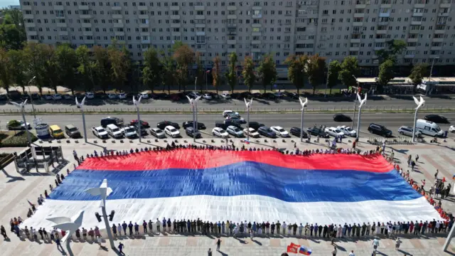Люди держат за края большое полотнище в цветах российского флага, вид сверху