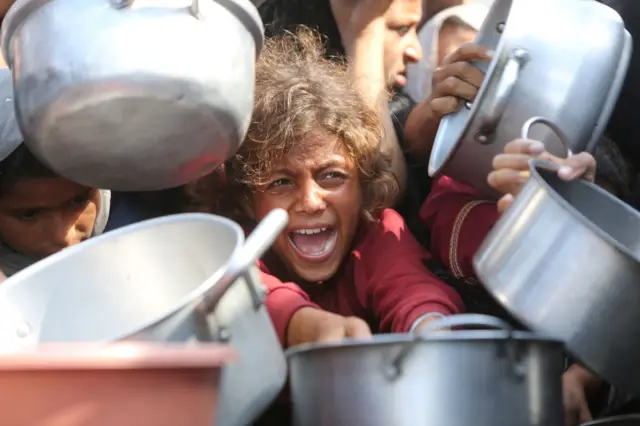 طفلة غزية تحمل وعاء وتحاول الحصول على الطعام بين جمع من الناس