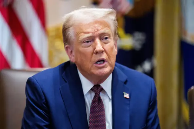 Трамп в синем пиджаке с красно-синим галстуком и значком в виде флажка США на лацкане