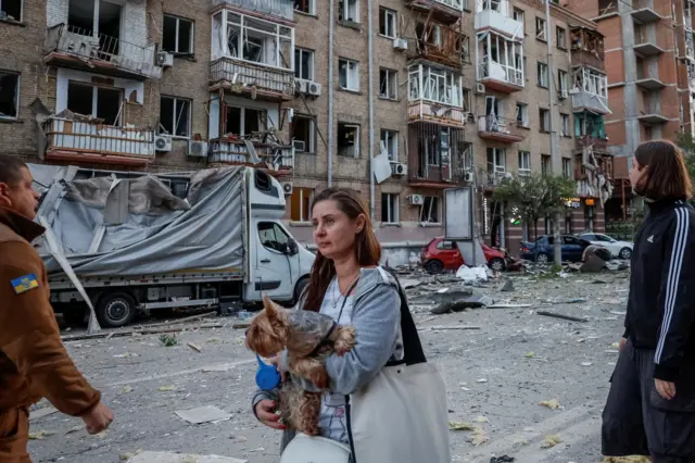 Женщина с собакой на фоне пострадавших домов