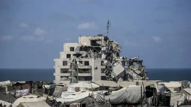 مبنى مدمر حوله خيام نازحين قبالة شاطئ غزة نهاراً