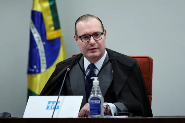 Zanin falando no julgamento; ele está sentado, em frente a bandeira dos EUA