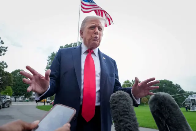 Дональд Трамп на фоне американского флага в синем пиджаке, белой рубашке и с красным галстуком